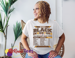 Woman wearing a white t-shirt with text about Black inventors, sitting in a chair with plants in the background.